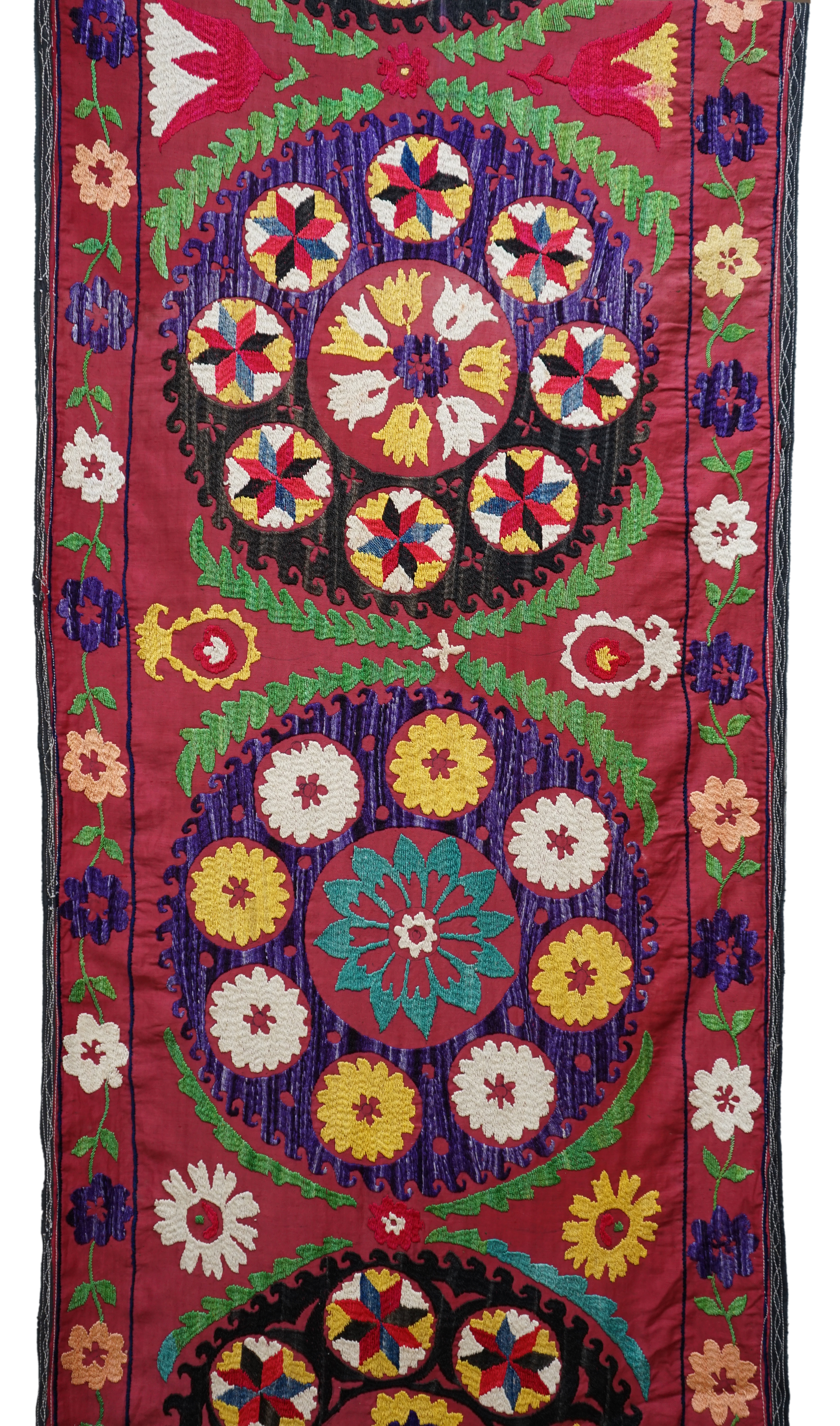 A 20th century Suzani wall hanging, possibly Uzbekistan, embroidered in bright polychrome silk threads into large symbols representing happiness, health and luck, on a burgundy cotton background, with a fine muslin backi